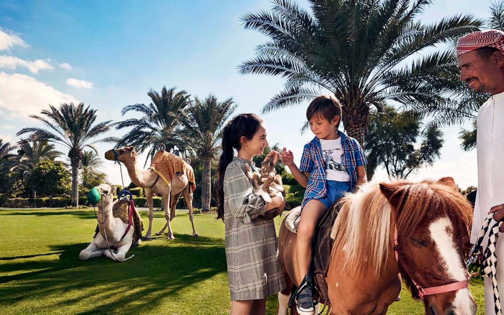 Kid riding a pony with a girl standing beside with a bunny in lap
