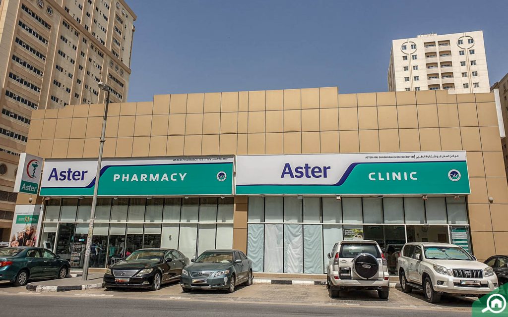 Exterior view of Aster Pharmacy and Clinic in Abu Shagara Sharjah with cars parked outside