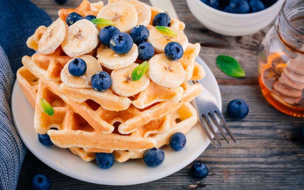 Plate of waffles with sliced bananas and whole blueberries