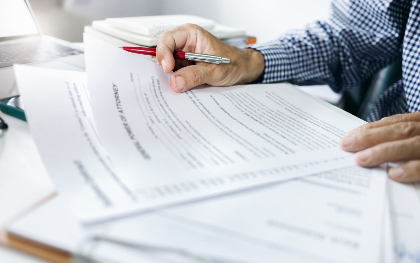 Close-up of a person holding a pen while reviewing legal Power of Attorney documents stacked on a desk.