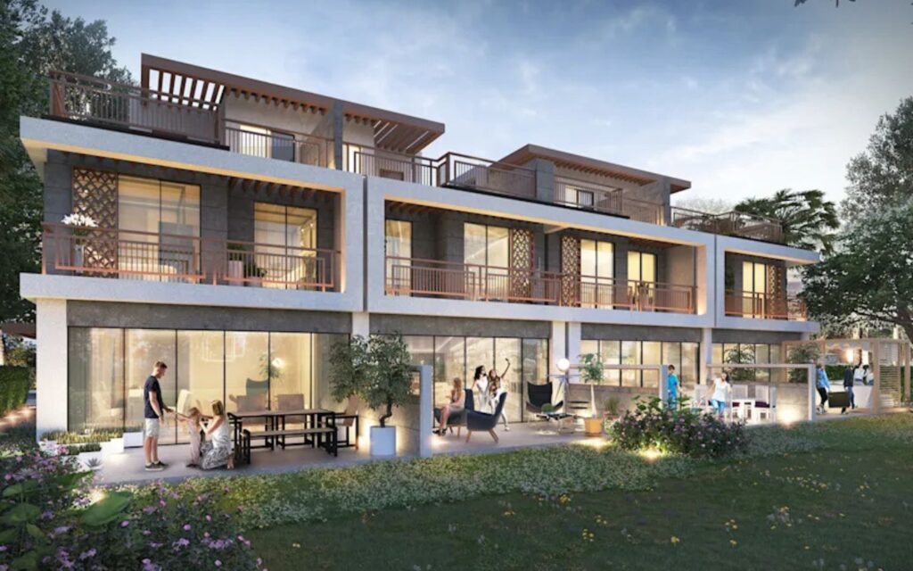 Modern multi-story luxury villas with large glass windows, rooftop terraces, and lit ground-floor patios facing a green lawn area.