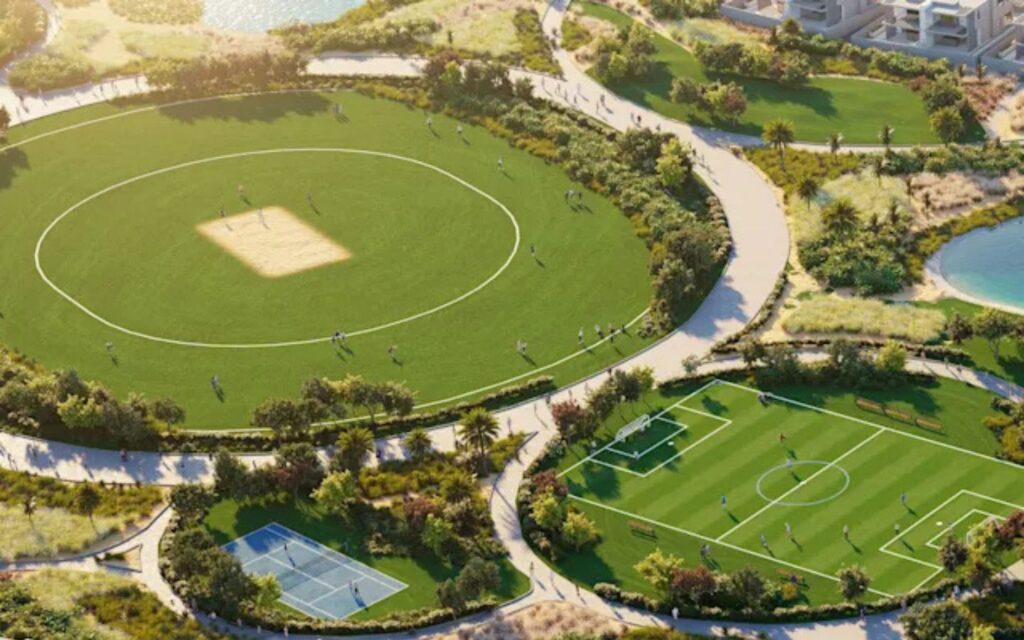 Bird's eye view of a green cricket ground and football field in DAMAC Hills 2