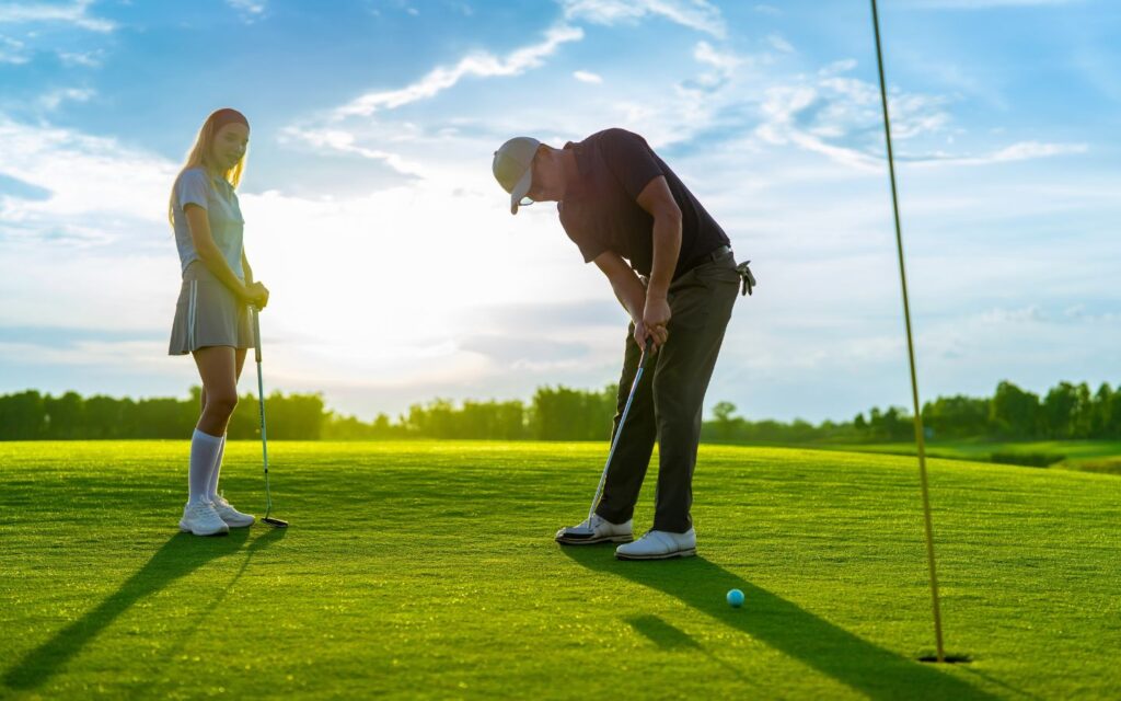 A man lines up a putt on a golf green while a woman watches from the side