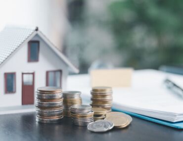 A small house model next to coin stacks showing salary needed to buy property in Dubai.