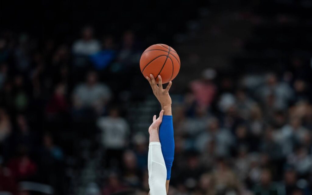 Two basketball players reaching for the ball during tip-off.