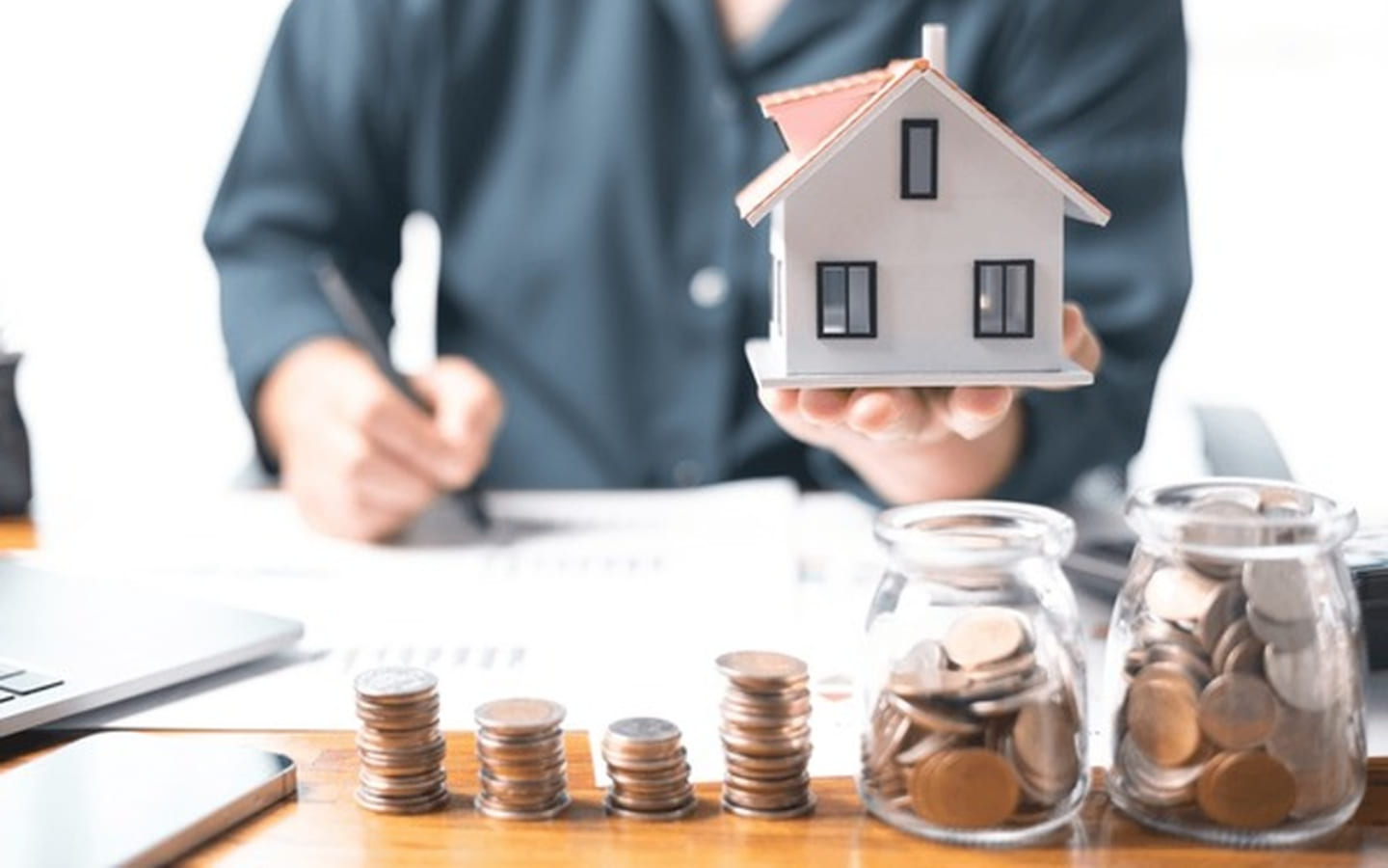 شخص يمسك مجسم بيت أمامه نقود