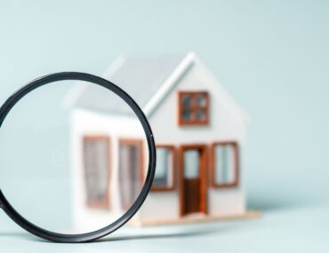 Magnifying glass focused on a small house model representing a property snagging inspection.