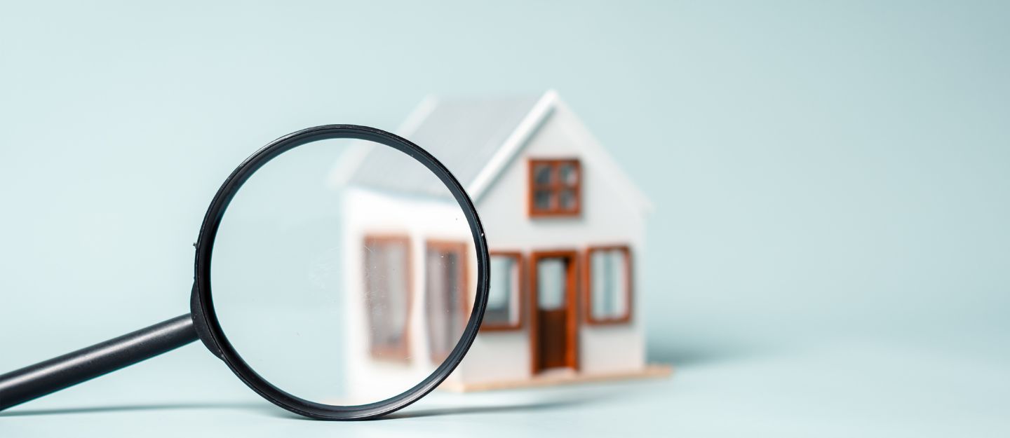 Magnifying glass focused on a small house model representing a property snagging inspection.