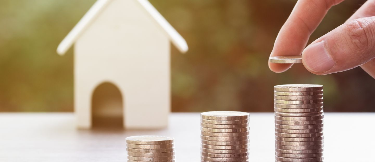 a person stacking coins in increasing order with a miniature house in the background