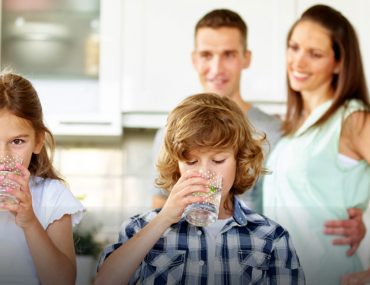 kids drinking water from glasses as parents watch in the background