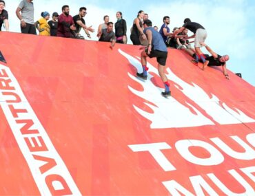 Team working together to climb an obstacle at the Tough Mudder Middle East challenge.