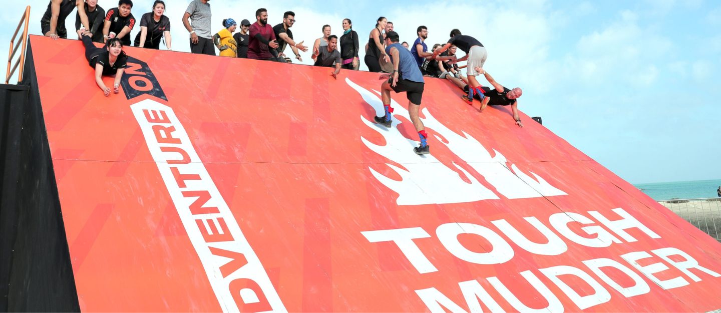 Team working together to climb an obstacle at the Tough Mudder Middle East challenge.