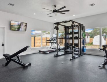 A garage conversion with heavy-duty rubber flooring, a matte black squat rack, and Olympic plates.