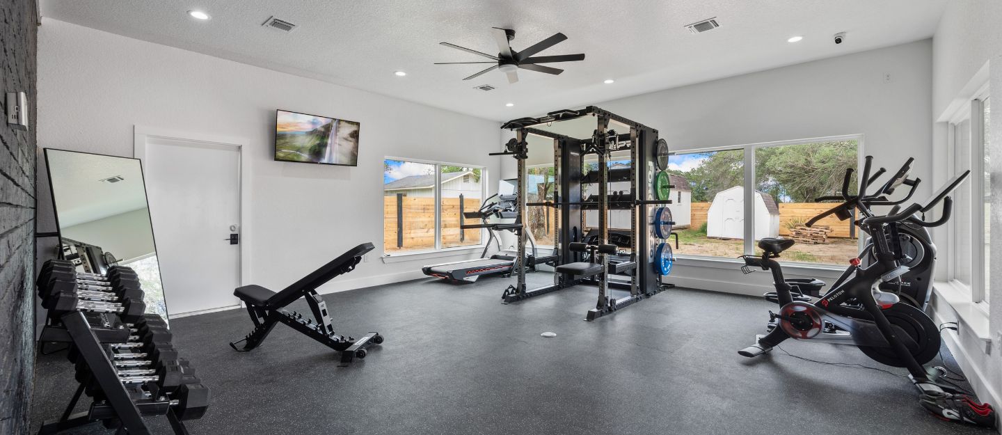 A garage conversion with heavy-duty rubber flooring, a matte black squat rack, and Olympic plates.