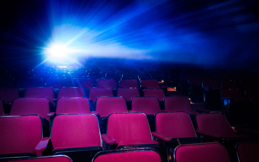 Empty movie theater seats with projector light shining.