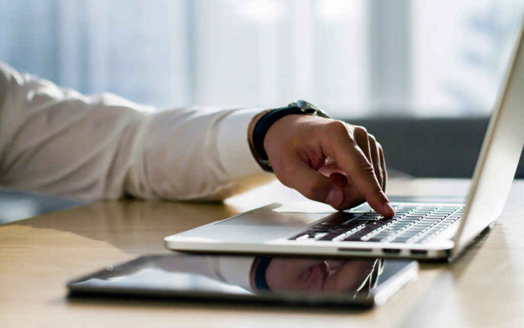 Close-up of businessman using laptop and tablet for online property transactions in the UAE.