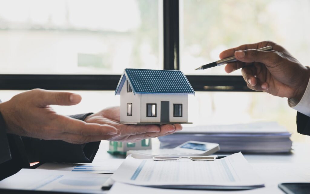 Two businessmen holding a mini house model across a table.