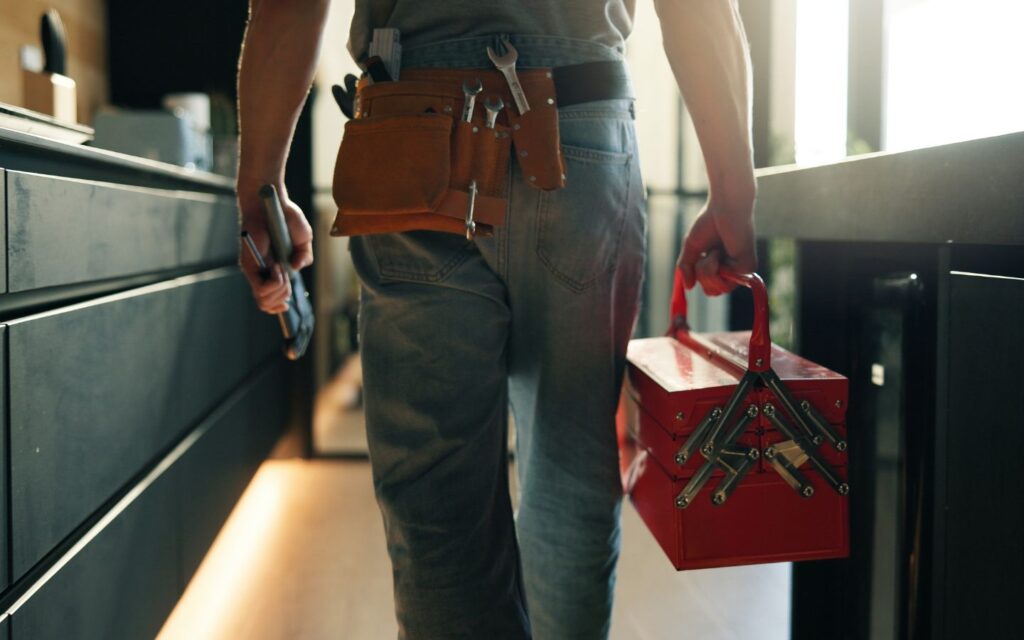 A handyman carrying a tool belt and red tool box.