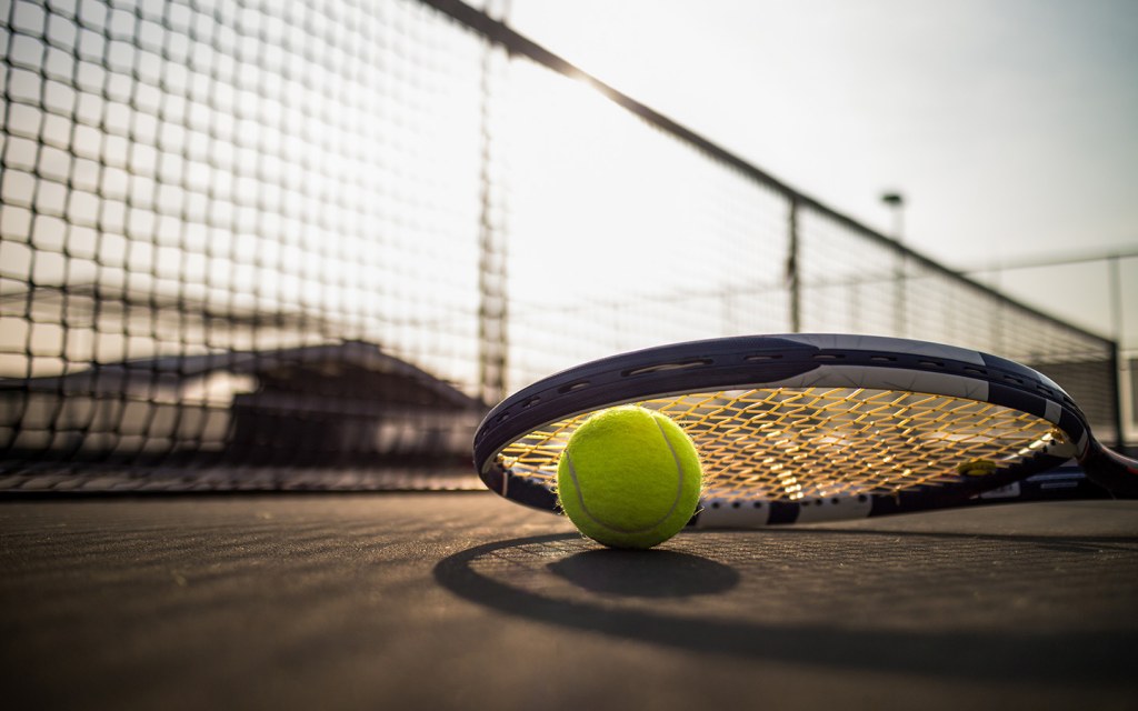 a tennis ball and a racket laying on the ground in a tennis court