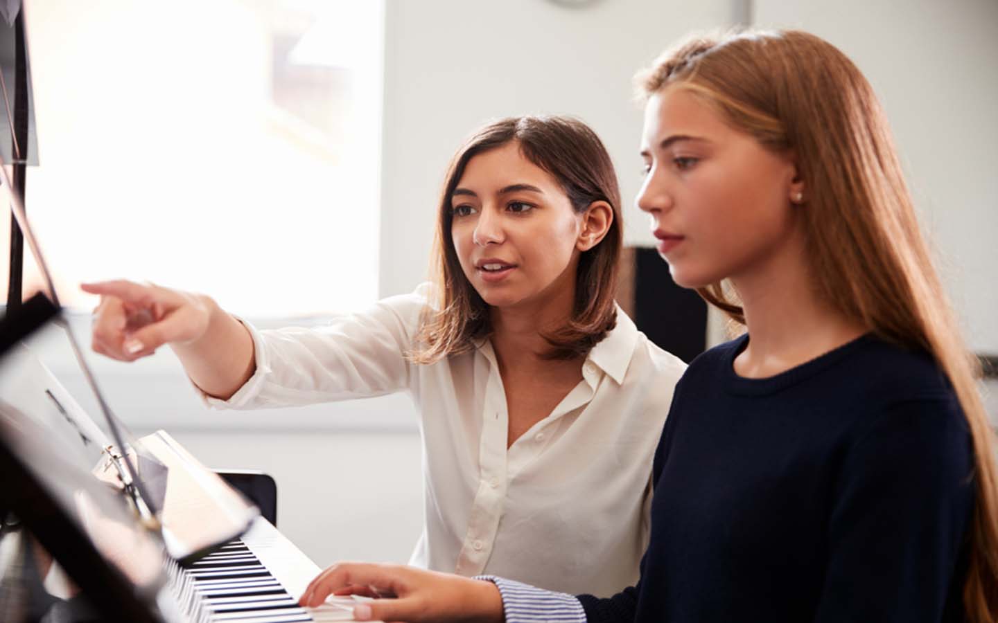 A teacher is giving piano lessons to the student