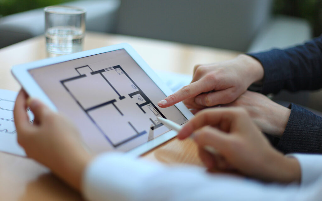 Hands reviewing a digital floor plan on a tablet during a real estate property discussion.