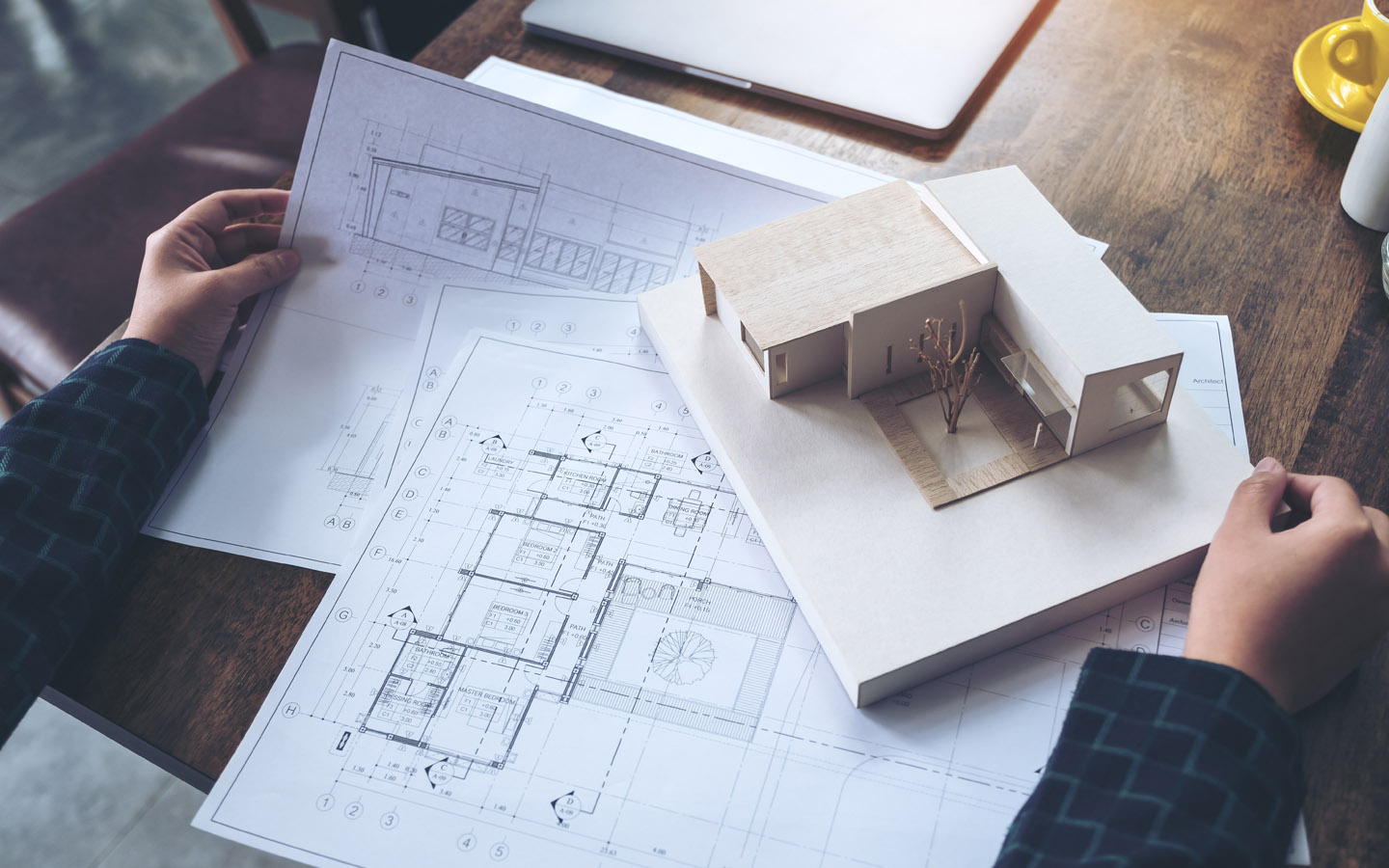 مهندس معماري يعمل وينظر إلى نموذج معماري مع ورق رسم على الطاولة